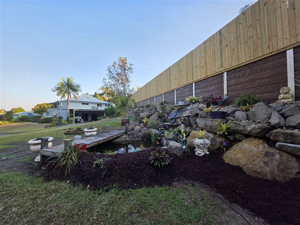 Sleeper and rock retaining walls with finished landscaping and a pond